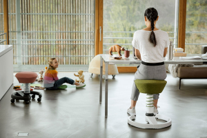 aeris Swopper (weißes Gestell und grüner Sitz) im Büro mit einer Frau